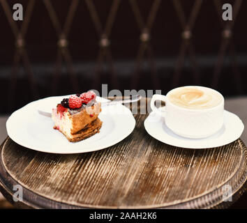 Patisserie Konzept. Käsekuchen mit Beeren und Kaffee auf Holztisch, aus der Nähe. Köstliches Dessert und Espresso auf Braun strukturierten Hintergrund. Stück Kuchen mit Brombeeren und Himbeeren. Stockfoto