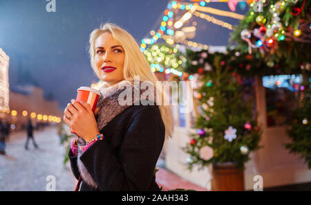 Bild des blonden Frau mit Glas in der Hand gegen den Hintergrund von brennenden Girlanden in der Straße am Abend Stockfoto
