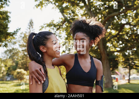 Fröhlicher junger sportlicher multiethnischen weibliche Freunde umarmen einander und lächelnd in den Park-glückliche Positiv mit Freunden im Park vor der Ausübung Stockfoto