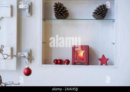 Unscharfe Red christmas Ball in einer Filiale vor einem Regal mit roten Weihnachtsdekoration, Laterne mit Kerze, rote Sterne, Tannen Zapfen Stockfoto