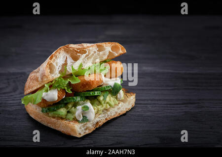 Appetitlich Sandwich auf einem Holzbrett. Baguette Sandwich mit Füllung aus Kopfsalat, Scheiben Tomate. Dunklen Hintergrund. Blick von oben. Close-up. Stockfoto