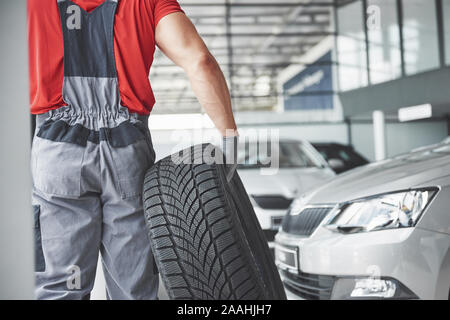 Nahaufnahme der Mechaniker Hände Schieben eines schwarzen Reifen in der Werkstatt Stockfoto