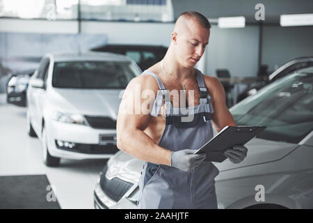 Ein hübscher junger Mann spricht in einem Autohaus, Instandsetzung, ein Auto in einer Werkstatt. Stockfoto