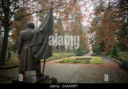 21 November 2019, Brandenburg, Potsdam: Die Bronze Skulptur oldat mit Fahne' ('Soldier mit Flagge"), der Bildhauer Walter Bullert 1953 entworfen, um die Gießerei Lauchhammer, vor einer Pergola auf der sowjetischen Friedhof in einem bewaldeten Gebiet steht auf der Bundesstraße 2 zwischen Potsdam und Michendorf. Auf 39 Grabstätten 2399 sowjetischen Krieg Toten aus dem Zweiten Weltkrieg und 2829 Offiziere, Soldaten, der zivilen Mitarbeiter und Offiziere der Garnison der sowjetischen Streitkräfte in der DDR begraben sind. An einigen Gräbern gibt es Bilder der Verstorbenen, eine Tradition, die in Russland üblich ist. Weitere Grabstein Stockfoto