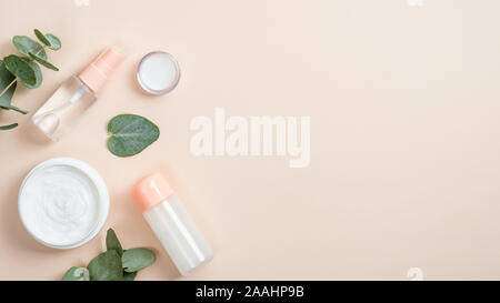 Kosmetische Flasche Behälter mit Öl und Glas mit weißen Hand Creme über beigen Hintergrund mit grünen pflanzliche Blätter. Natürliche Schönheit Produkt con Stockfoto