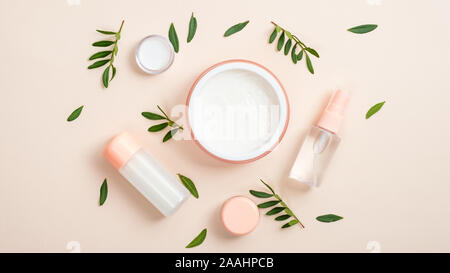 Organische Kosmetik Flasche Container und Glas mit weißen Gesicht Creme auf beigen Hintergrund mit grünen pflanzliche Blätter. Kreative Gestaltung, minimale flach Stil Stockfoto
