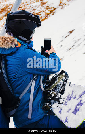 Sport Mädchen Snowboarder in Helm und Maske nimmt Bilder mit Smartphone, sitzen auf Kabel weg. Reisen Lifestyle Sport und Extreme, Abenteuer Aktivitäten Stockfoto
