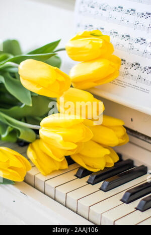 Gelbe Tulpen auf einem weißen Piano mit Notizen Stockfoto