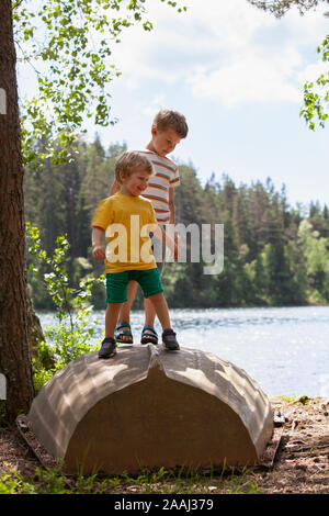 Spielen Brüder auf den Kopf Boot in der Nähe von See, Finnland Stockfoto