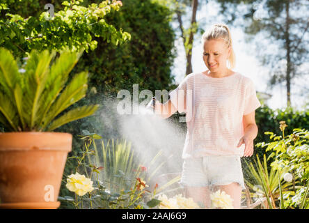 Bewässerung Frau Pflanzen mit Wasser Schlauch im Garten Stockfoto