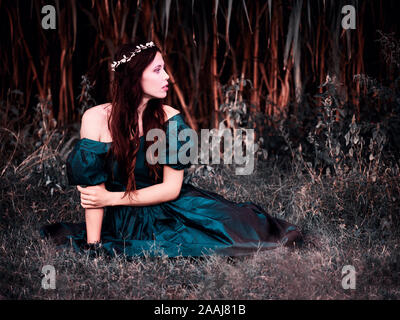 Schöne junge Frau sitzt im Gras tragen Vintage grüne Kutte Stockfoto