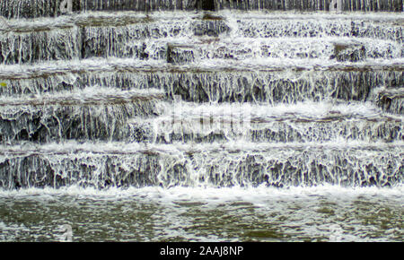 Wasser Kaskadierung über Wehr Schritte auf Canal Helling, blur unscharf Bewegungs- und freeze frame von Wassertröpfchen für Hintergrund tectures und Layer Effe Stockfoto
