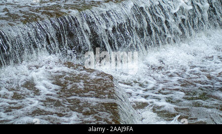 Wasser Kaskadierung über Wehr Schritte auf Canal Helling, blur unscharf Bewegungs- und freeze frame von Wassertröpfchen für Hintergrund tectures und Layer Effe Stockfoto