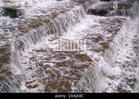 Wasser Kaskadierung über Wehr Schritte auf Canal Helling, blur unscharf Bewegungs- und freeze frame von Wassertröpfchen für Hintergrund tectures und Layer Effe Stockfoto