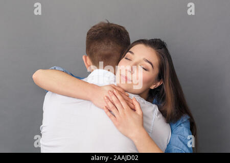 Beziehung Konzept. Junges Paar umarmen lächelnde Frau reizvolle Studio stehen isoliert auf Grau Stockfoto