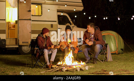 Gruppe von Freunden um brennende camping Feuer in den Wäldern Marshmallows rösten. Retro Wohnmobil. Stockfoto