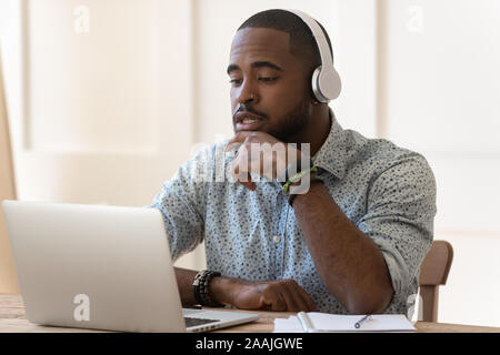 Konzentriert biracial Mann in Kopfhörer ansehen Webinar am Laptop Stockfoto