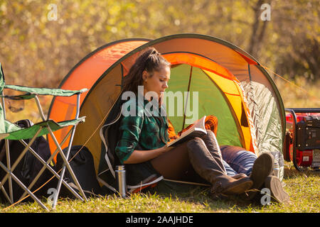 Junge Mädchen beim Lesen eines Buches vor dem Zelt. Wilde Atmosphäre Stockfoto