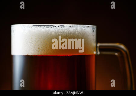Dunkle Bierkrug mit weißer Schaum auf dunklem Hintergrund Nahaufnahme Stockfoto