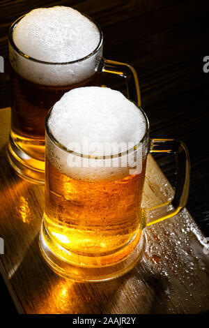 Zwei helle Bier Becher mit weißer Schaum auf dunklen Holztisch. Ansicht von oben Stockfoto