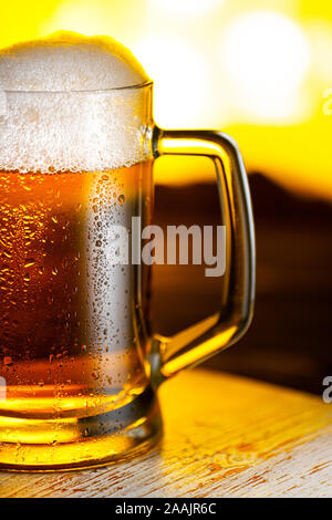 Licht Bierkrug mit weißer Schaum auf Holztisch und gelbem Hintergrund Nahaufnahme Stockfoto