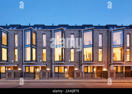 Frontansicht der modernen Terrasse mit beleuchteten Innenräumen. Warriner Gardens, London, Vereinigtes Königreich. Architekt: Kind Graddon Lewis, 2019. Stockfoto