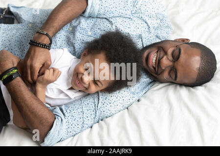 Ansicht von oben liebenden Vater kitzelt kleinen Sohn liegend auf Bett Stockfoto