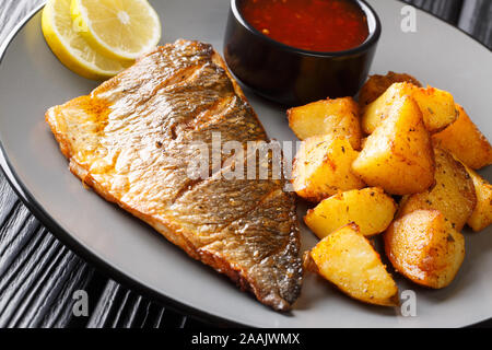 Gebratene vergoldeten Kopf Fischfilet mit Kartoffeln und Saucen close-up auf einem Teller auf den Tisch. Horizontale Stockfoto