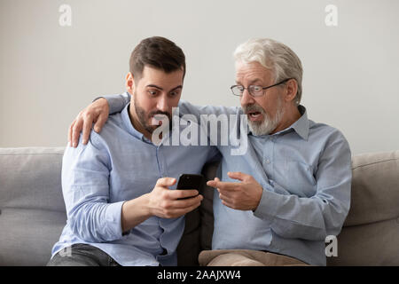 Alten Vater und mit Phone Sohn, durch unerwartete Nachrichten schockiert Stockfoto