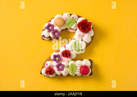 Nummer zwei Kuchen geschmückt mit Blumen und macarons auf gelbem Hintergrund Stockfoto