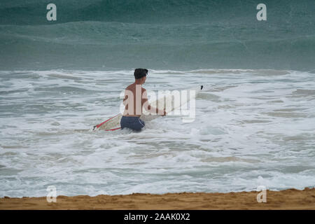 Junger Mann mit Surfbrett im Meer im Regen laufen Stockfoto