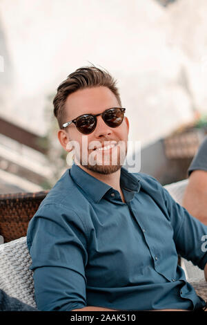 Portrait Bild der junge Mann im blauen Hemd in die Kamera schaut. Gut aussehender Geschäftsmann Sonnenbrille tragen. Gut aussehenden Mann lächelnd. Stockfoto