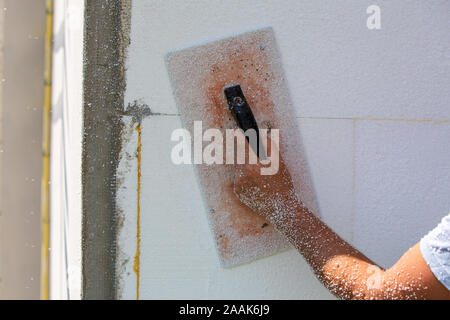 Hand eines Arbeitnehmers mit einem Werkzeug zum Schleifen und Glätten und sogar die Oberfläche einer Hauswand mit Styrofoam Dämmplatten isoliert. Stockfoto