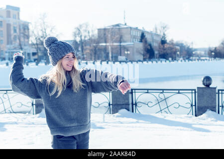 Porträt einer Frau, die der Vorbereitung einer schneeball vor dem Hintergrund einer zugefrorenen Fluss im Winter Stadt zu werfen Stockfoto