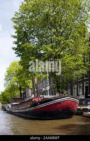 Blick auf den Kanal, Boot Haus, Bäume und historischen, traditionellen Gebäuden, die niederländische Architektur in Amsterdam. Es ist ein sonniger Sommertag. Stockfoto