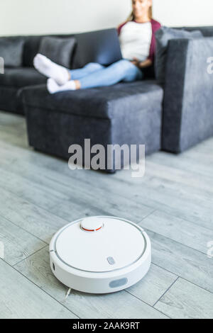 Roboter Staubsauger Reinigen der Zimmer, während Frau ruht auf dem Sofa Stockfoto