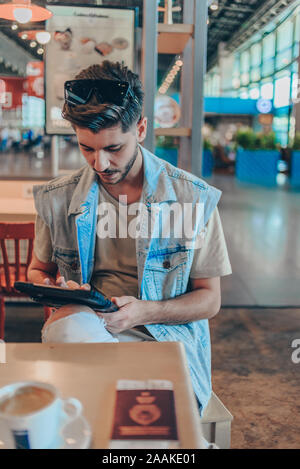 Caredree Mann die Arbeit auf Tablet am Flughafen Bahnhof während seiner Flucht warten Stockfoto