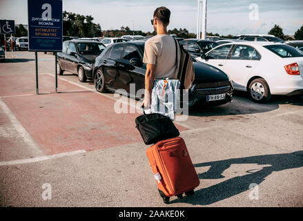 Rückansicht des zuversichtlich, dass man in lockerer Kleidung entlang Lounge im Flughafen, während sein Gepäck tragen Stockfoto