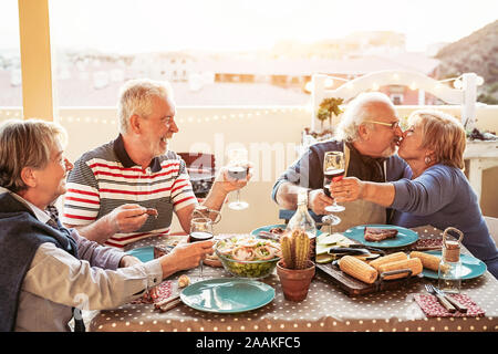 Gerne ältere Freunde Ess- und jubeln mit Rotwein am Grill auf der Terrasse im Freien - pensionierte Menschen, die Spaß an der Grillparty auf der Terrasse Stockfoto