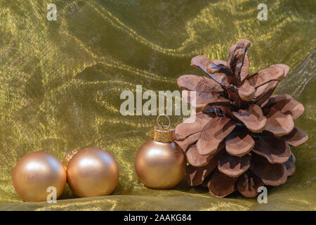 A Pine Cone und goldenen Weihnachtsbaum Kugeln auf einem farbigen Tuch. Stockfoto