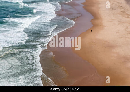 Einsamer single Person zu Fuß entlang der Uferpromenade von leeren Sandstrand Praia Grande in der Nähe von Sintra Portugal im Sommer Stockfoto