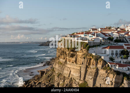 Azenhas do Mar eingebettet auf Klippen oberhalb der Atlantikküste in Portugal in der Nähe von Sintra mit Wellen, die sich im rollenden unter blauem Himmel Stockfoto