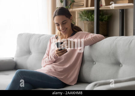 Lächelnde Mädchen sitzen auf dem Sofa, die angenehme Nachricht auf dem Smartphone Stockfoto