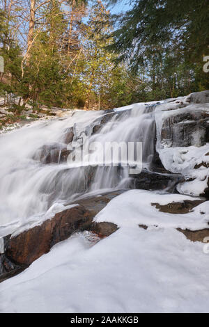 Kaltes Wasser purzelt in den Granitfelsen in Eis und Schnee bedeckt, an der Fischzuchtanstalt fällt in Huntsville, Ontario. Stockfoto