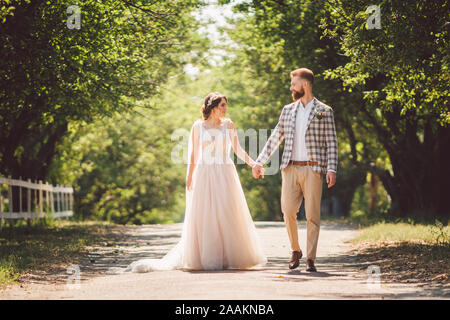 Hochzeit paar genießt, zu gehen in den Wald. Brautpaar umarmen und halten Händchen. Brautpaar zu Fuß nach vorne, die Hand im Park auf dem Weg in den sonnigen Stockfoto