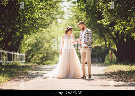 Hochzeit paar genießt, zu gehen in den Wald. Brautpaar umarmen und halten Händchen. Brautpaar zu Fuß nach vorne, die Hand im Park auf dem Weg in den sonnigen Stockfoto