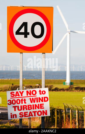 Ein Protest Zeichen über eine neue Windenergieanlage im Seaton in der Nähe von Workington, Cumbria, Großbritannien, bei auflandigem Wind Turbinen und die Offshore- Windpark "Robin Rigg visib Stockfoto