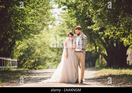 Hochzeit paar genießt, zu gehen in den Wald. Brautpaar umarmen und halten Händchen. Brautpaar zu Fuß nach vorne, die Hand im Park auf dem Weg in den sonnigen Stockfoto