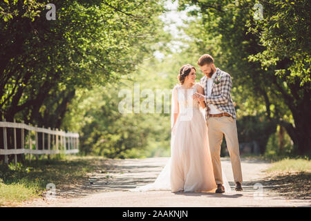 Hochzeit paar genießt, zu gehen in den Wald. Brautpaar umarmen und halten Händchen. Brautpaar zu Fuß nach vorne, die Hand im Park auf dem Weg in den sonnigen Stockfoto