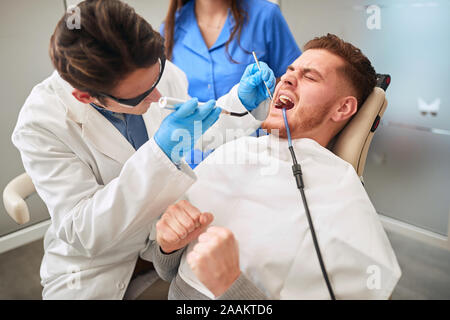 Zahnärzte bei der Arbeit. regelmäßigen Zahnarzt besuchen. junger Mann Zahn Schmerzen leiden. Stockfoto